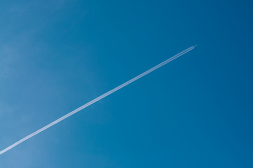 Airplane flying through clear blue sky with vapour trails