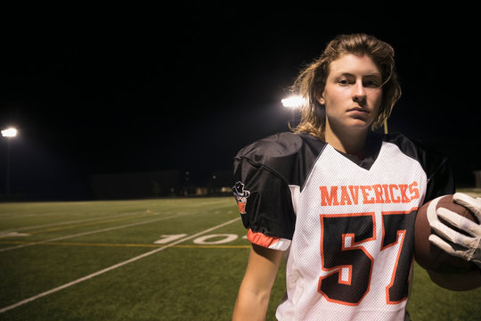 Portrait confident, tough teenage boy high school football player on football field at night