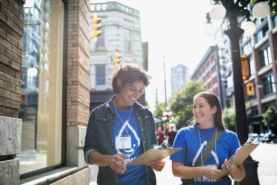 Smiling political young adults canvassing with clipboards on sunny urban sidewalk