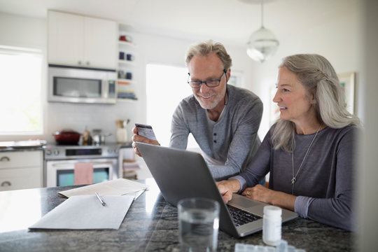 Senior couple with credit card paying bills at laptop in kitchen