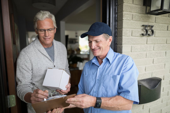 Senior Man Signing Clipboard For Box Package For Delivery Man At Front Door