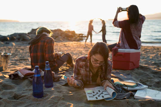 Brother And Sisters Relaxing, Photographing With Camera Phone And Doing Crossword Puzzle On Sunny Ocean Beach