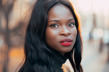 A beautiful young black African girl with a happy smile poses outdoors in the rays of the setting...