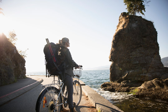 Woman with hiking backpack and bicycle looking at sunny ocean view