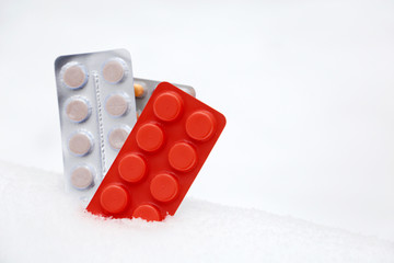Pills in blister packs in the snow, different cooled medication close-up. Concept of pharmacy, vitamins in cold and flu season, health care in winter