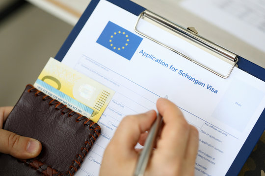 Top view of man filling out documents for Schengen visa while holding money. Travel concept