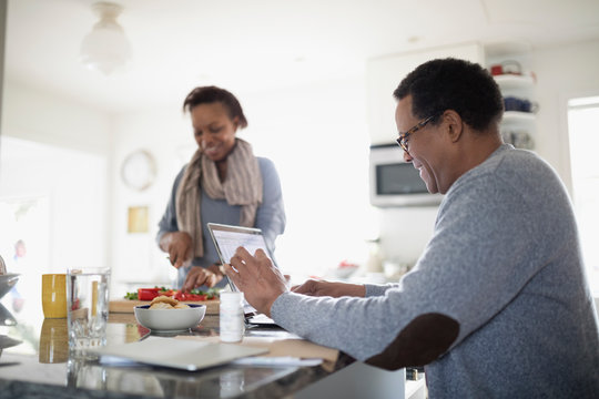 Senior Couple Cooking And Using Laptop In Kitchen