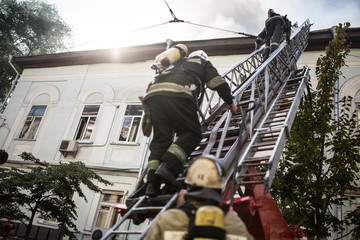 Firefighters on ladders in oxygen masks extinguish the fire in an old house in the middle of the...