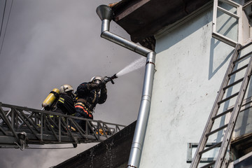 Firefighters on ladders in oxygen masks extinguish the fire in an old house in the middle of the city