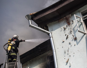 Firefighters on ladders in oxygen masks extinguish the fire in an old house in the middle of the...