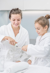 Fototapeta premium Happy woman squeezes toothpaste onto toothbrush for her daughter in bathroom at home