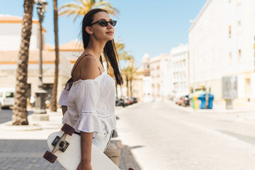 girl in sunglasses with a skateboard mouse looks over her shoulder in the sunny city of Spain