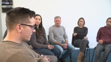 4K: Support group therapy - People sat in circle for a recovery meeting - One man talks while the others listen. 