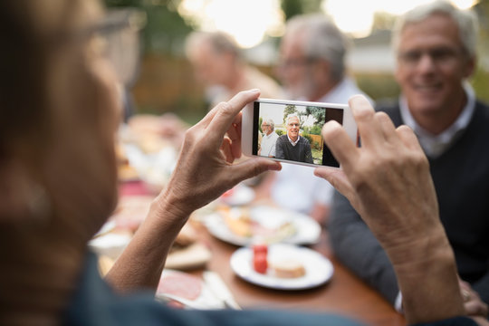Senior woman photographing husband with camera phone at patio table