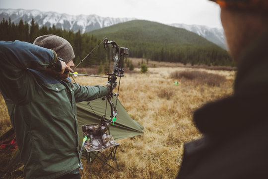 Male hunter aiming hunting compound bow in remote field below mountains