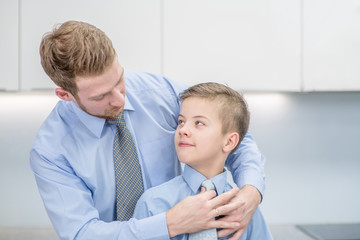 Father helps his son to tying necktie at home