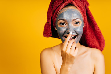 girl with a black mask on her face, puts a finger to her nose and smiles joyfully. background yellow