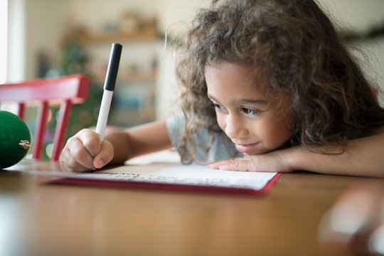 Smiling Girl Writing Christmas Letter To Santa At Table