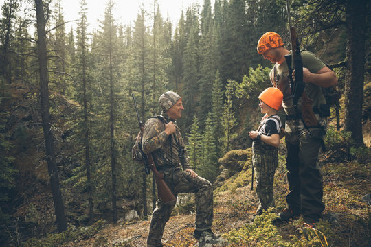 Multi-generation male hunters with hunting rifles talking on forest ridge