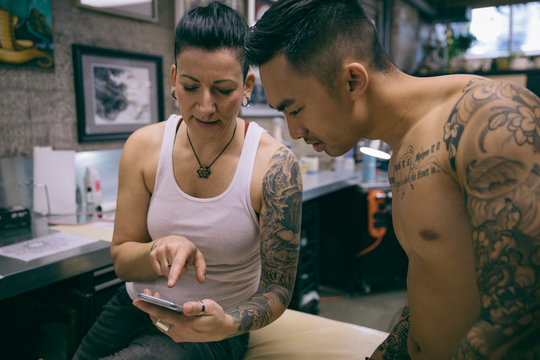 Tattoo artist and client using smart phone in tattoo studio