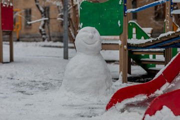 A snowman is standing on the playground. Winter, snowfall.