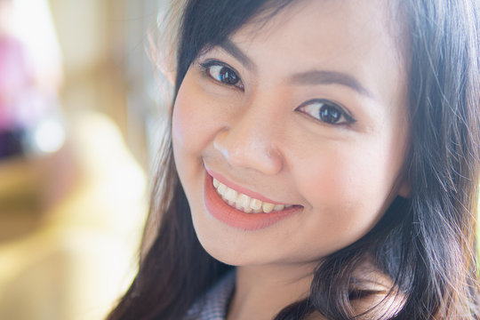 A close up head shot portrait of young Asian woman smiling happily.