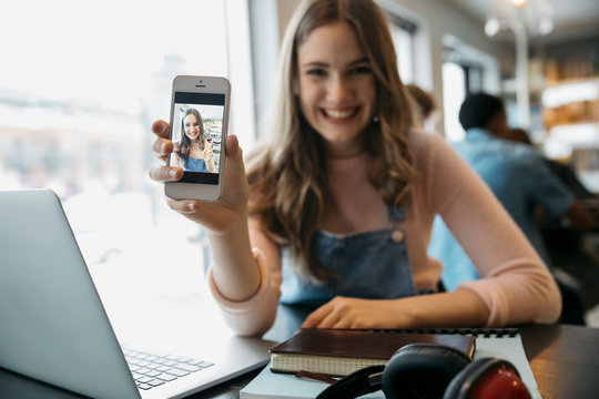 Portrait smiling, confident tween girl showing selfie on camera phone at laptop in cafe