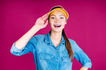 the girl smiles joyfully and touches the visor on her head with her hand. background pink