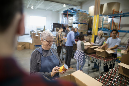 Senior woman filling donation boxes with canned Food for Food drive in warehouse