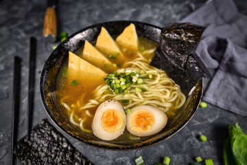 Homemade vegetarian Japanese Ramen noudle soup with fried tofu slices, egg and spring onions in dark bowl