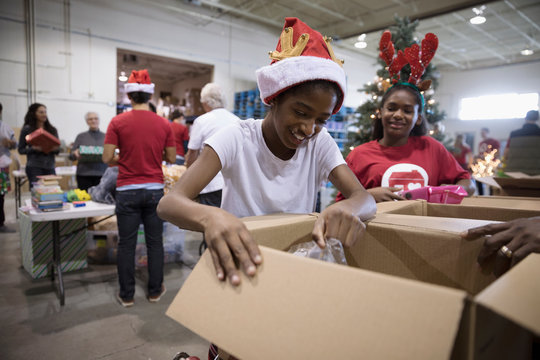Smiling girl volunteer in Santa hat filling donation box in warehouse