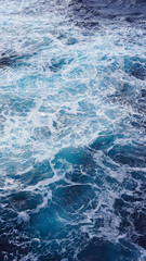 Dark water of the pacific ocean. Natural blue background. foam composition in the ocean. white sea foam, waves, storm. vertical photo