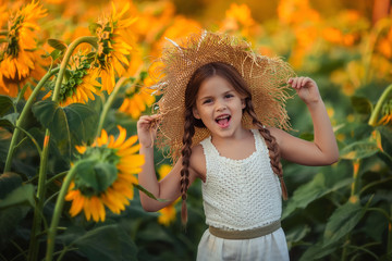 Portrait of a beautiful cheerful girl in a straw hat on a field of sunflowers.