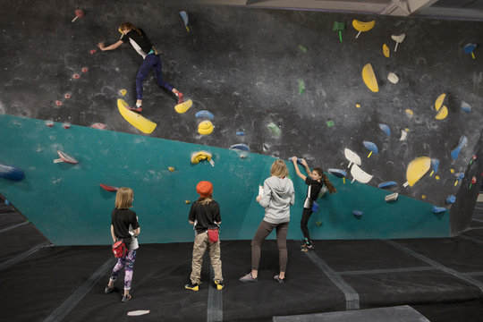 Female instructor and rock climbing students watching girl climbing wall at climbing gym