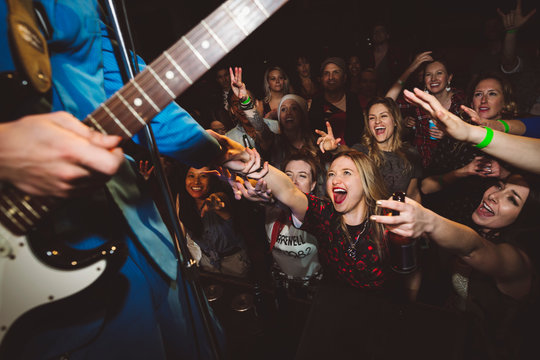 Enthusiastic young female milennials in crowd cheering and reaching for rockabilly musician on stage