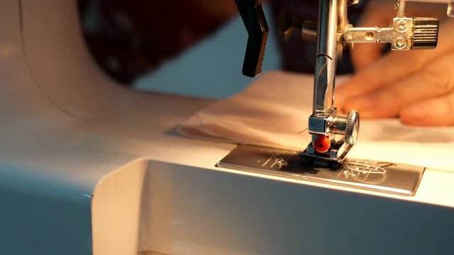 Tailoring Process - Womens hands using sewing machine with light of built-in lamp, that would making textile clothes. Needle with looper and presser foot. Handcraft concept.