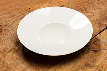 Plato blanco redondo hondo sobre mesa de madera rústica. Vista superior