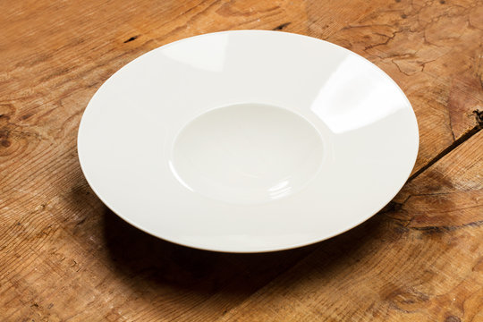 Plato blanco redondo hondo sobre mesa de madera r&uacute;stica. Vista superior