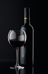 Bottle and glass of red wine on a black background.