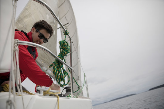 Man adjusting rigging rope on sailboat on ocean