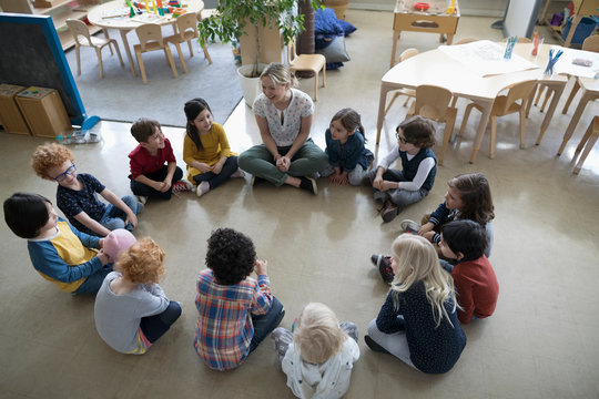 Preschool teacher and students sitting in circle on floor in classroom