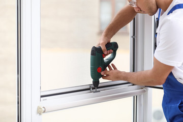 Construction worker repairing plastic window with electric screwdriver indoors