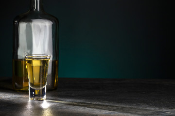 Portion of strong alcohol is brightly illuminated and half a bottle behind it on a beautiful dark background. Copy space.