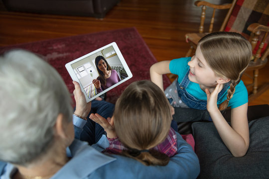 Grandmother and granddaughters video chatting with digital tablet on sofa