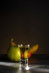 Close-up shot of whiskey and fruit behind it on a beautiful dark brown background. Vertical. Copy space.