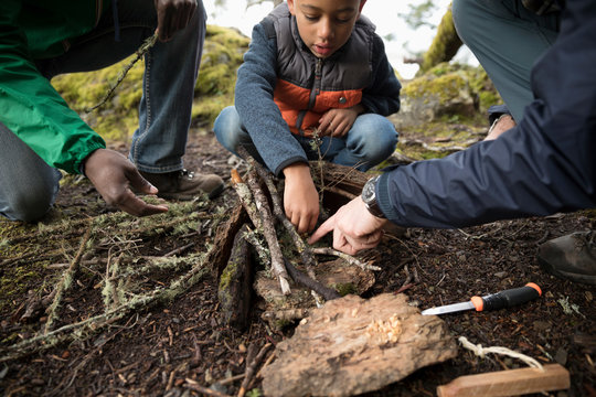 Trail guide and father helping boy build a fire in woods