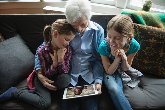 Grandmother and granddaughters video chatting with digital tablet on sofa