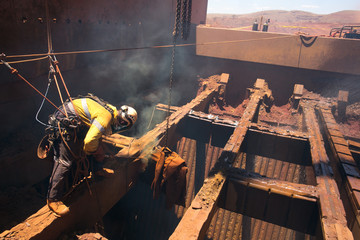 Rope access boilermaker abseiler wearing safety harness, helmet standing on beam structure using...