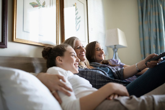 Affectionate mother and teenage daughters watching TV on bed