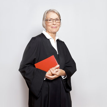 Best Legal Advice Concept: Portrait Of A Friendly Smiling Mature Woman With Law Book In A Black Judge's Gown.